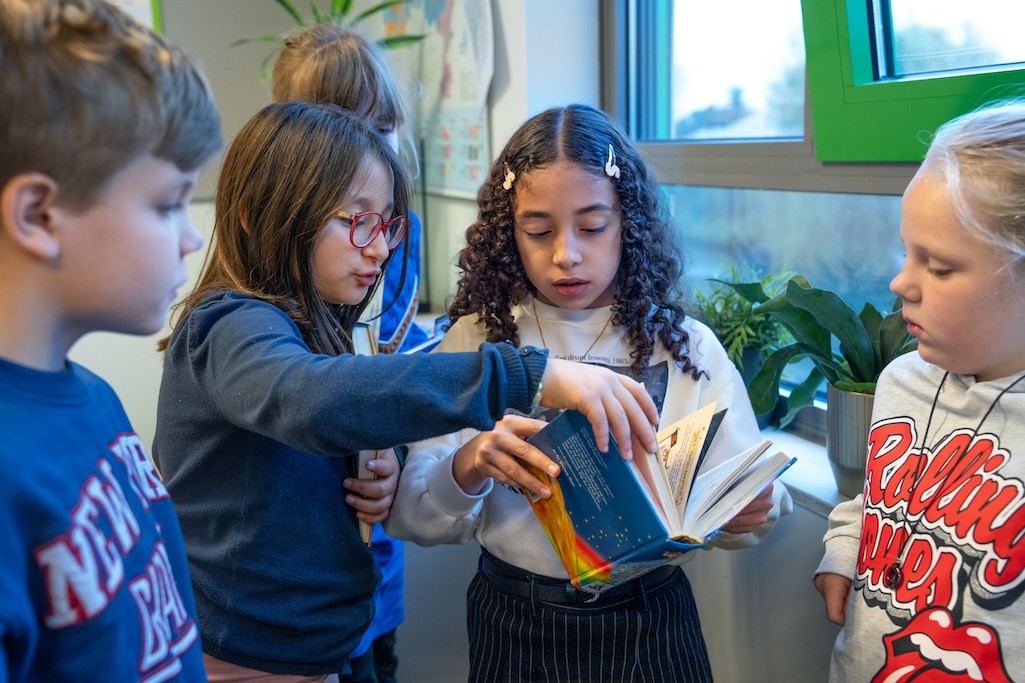 Kinderen bladeren samen door een boek, staand in een lokaal.
