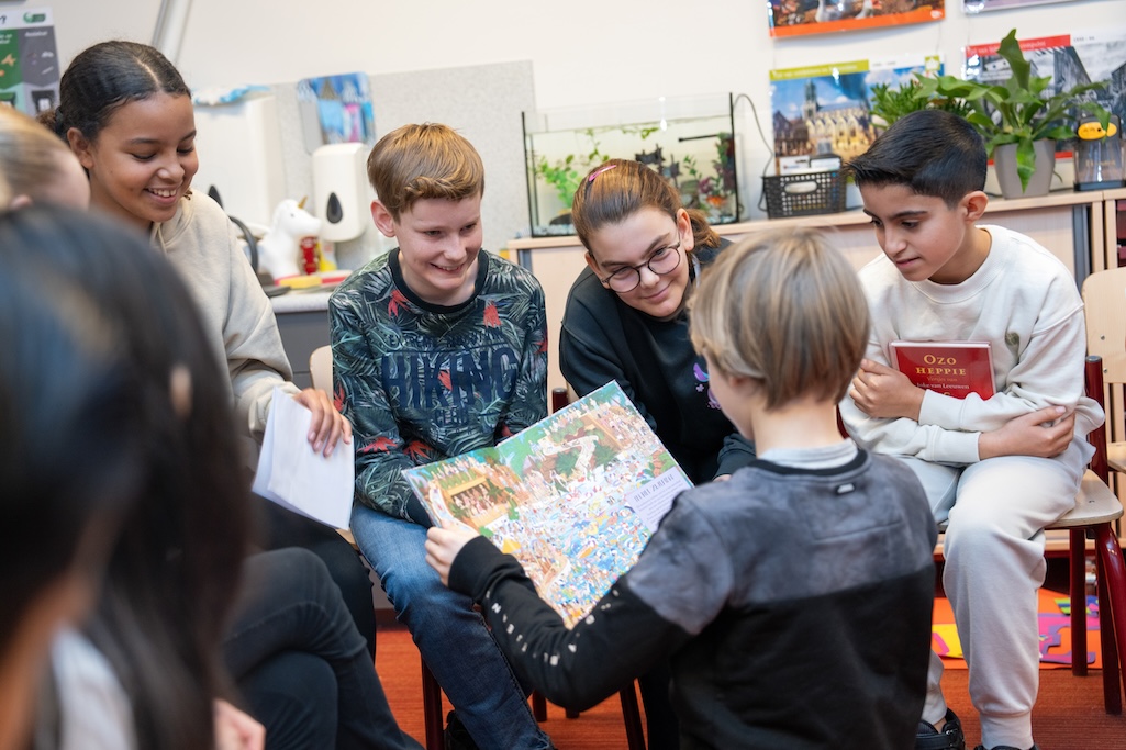 Kinderen zitten in een kring, er wordt een boek gepresenteerd